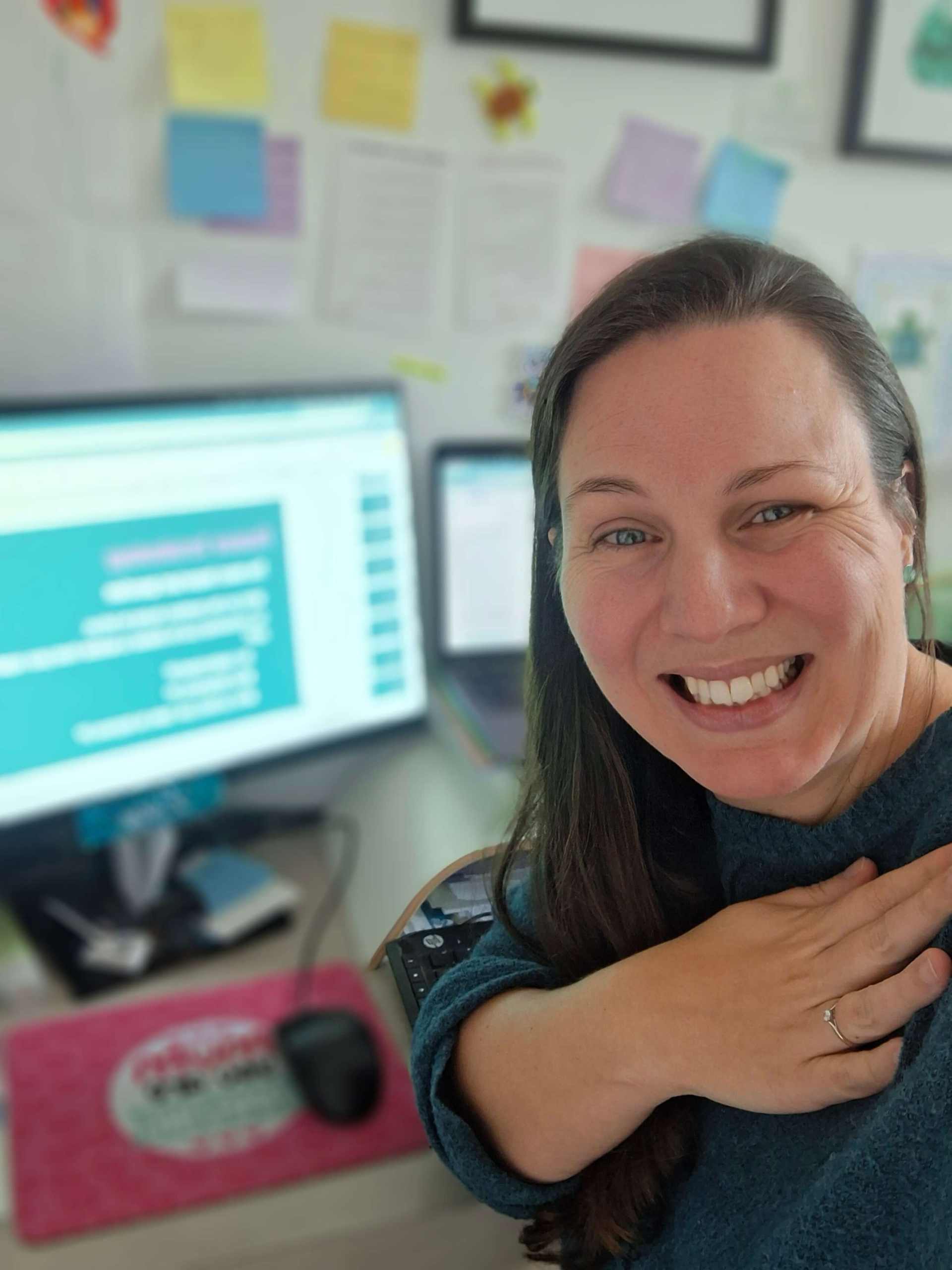 A photo of Lucy feeling very proud of the participants in front of monitors showing Clarity Circle content